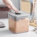 A hand pressing a OXO Good Grips plastic container with brown powder using a stainless steel button.