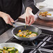A person cooking food in a Vollrath aluminum non-stick fry pan.