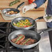 A woman cooking food in a Vollrath Wear-Ever non-stick frying pan on a stove.