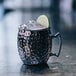 A metal Arcoroc Hammered Black Moscow Mule Mug with ice and a lime wedge on a table.