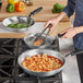 A woman using tongs with a Vollrath Wear-Ever frying pan with a black handle to cook meat.