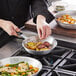 A person cooking food in a Vollrath aluminum fry pan.