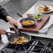 A person cooking food in a Vollrath stainless steel frying pan.