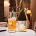 Two Arcoroc Precision Double Old Fashioned glasses with ice and amber liquid on a table.