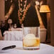 An Arcoroc double old fashioned glass filled with ice and whiskey on a table in a cocktail bar.