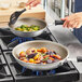 A hand stirring vegetables in a Vollrath Wear-Ever non-stick fry pan on a stove.