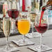 A bartender pours red wine into Arcoroc wine glasses on a table.