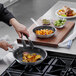 A person cooking food in a Vollrath Arkadia frying pan.