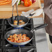 A person cooking shrimp in a Vollrath non-stick fry pan on a stove.