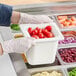 A person in gloves holding a Carlisle white container of vegetables at a salad bar.