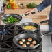 A person cooking food on a stove with Vollrath Tribute stainless steel frying pans.