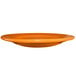 An orange International Tableware stoneware plate with a rolled edge on a white background.