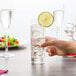 A hand holding an Arcoroc Islande highball glass filled with water and ice with a lime wedge on top.