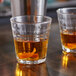 Two Duralex stackable glass tumblers filled with liquid and garnished with orange peel on a table.
