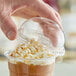 A hand placing a Dart plastic dome lid with a hole on a cup of coffee.