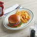 A Tuxton oval china platter with a hamburger and fries on it.