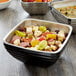 A Vollrath black metal bowl filled with food on a table.