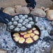 A Lodge cast iron skillet with a pie cooking over a campfire.