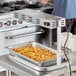 An Avantco French fry dump station with a silver pan of french fries on a counter.