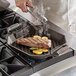 A person using a FINEX octagonal cast iron grill pan to cook a steak on a grill.