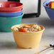 A bowl of soup with a spoon in an assorted color melamine bouillon cup.