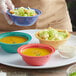 A person holding a bowl of salad with a clear bowl of soup on a table with three bowls of food.