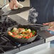 A person cooking food in a FINEX cast iron skillet on a stove.