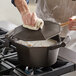 A man stirring soup in a FINEX cast iron Dutch oven on the stove.