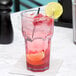 A Carlisle clear plastic tumbler with a pink drink, straw, and a slice of lime.