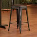 A Lancaster Table & Seating black backless counter height stool with a walnut seat.