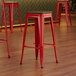 A red Lancaster Table & Seating backless barstool with a walnut wood seat.