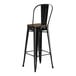 A black metal Lancaster Table & Seating barstool with a walnut wood seat.