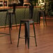 A Lancaster Table & Seating black metal barstool with a walnut wood seat.