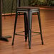 A Lancaster Table & Seating black backless counter height stool with a walnut wood seat.