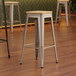 A set of three Lancaster Table & Seating metal barstools with natural wood seats.