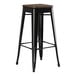 A Lancaster Table & Seating black metal backless barstool with a walnut wood seat.