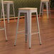 Three Lancaster Table & Seating nickel gray metal bar stools with natural wood seats.