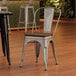 A Lancaster Table & Seating silver metal cafe chair with a walnut wood seat sits in front of a table.