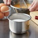 A person whisking eggs in a Vollrath stainless steel mixing bowl on a counter.