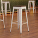 Three Lancaster Table & Seating pearl white metal barstools with walnut seats.