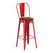 A red Lancaster Table & Seating metal bar stool with a walnut wood seat.