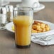 A Carlisle smoke plastic tumbler filled with orange juice sits on a table next to a plate of breakfast food.