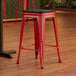 A red Lancaster Table & Seating backless counter height stool with a black wood seat.