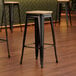 A Lancaster Table & Seating black metal barstool with a natural wood seat.