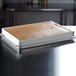 A rectangular white fiberglass sheet pan extender on a metal tray with brown substance inside.