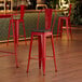 A Lancaster Table & Seating Ruby Red Cafe Barstool with Black Wood Seat at a table in a bar.