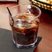 A Carlisle clear plastic tumbler filled with brown liquid and ice with a straw.