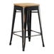 A black metal Lancaster Table & Seating counter height stool with a natural wood seat.