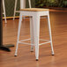 A white Lancaster Table & Seating backless counter height stool with a natural wood seat.