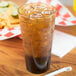 A Carlisle amber plastic tumbler filled with brown liquid and ice on a table with fries and a straw.